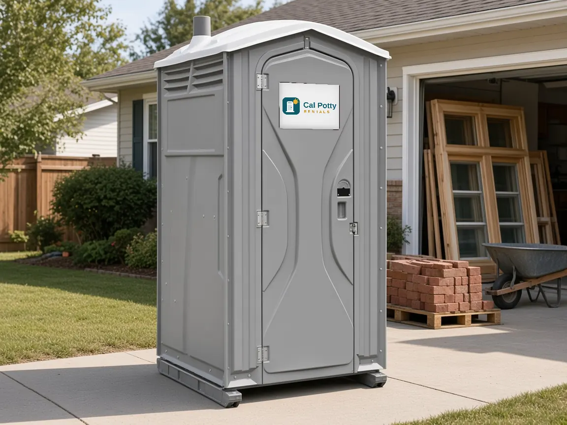 A grey porta potty at a driveway remodel with window frames and bricks, an example setup for porta potty rental in Cupertino
